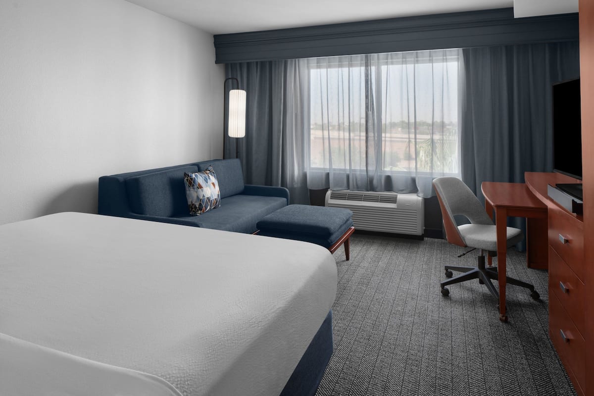 A hotel room with a large bed, a sofa, a desk, and a chair.