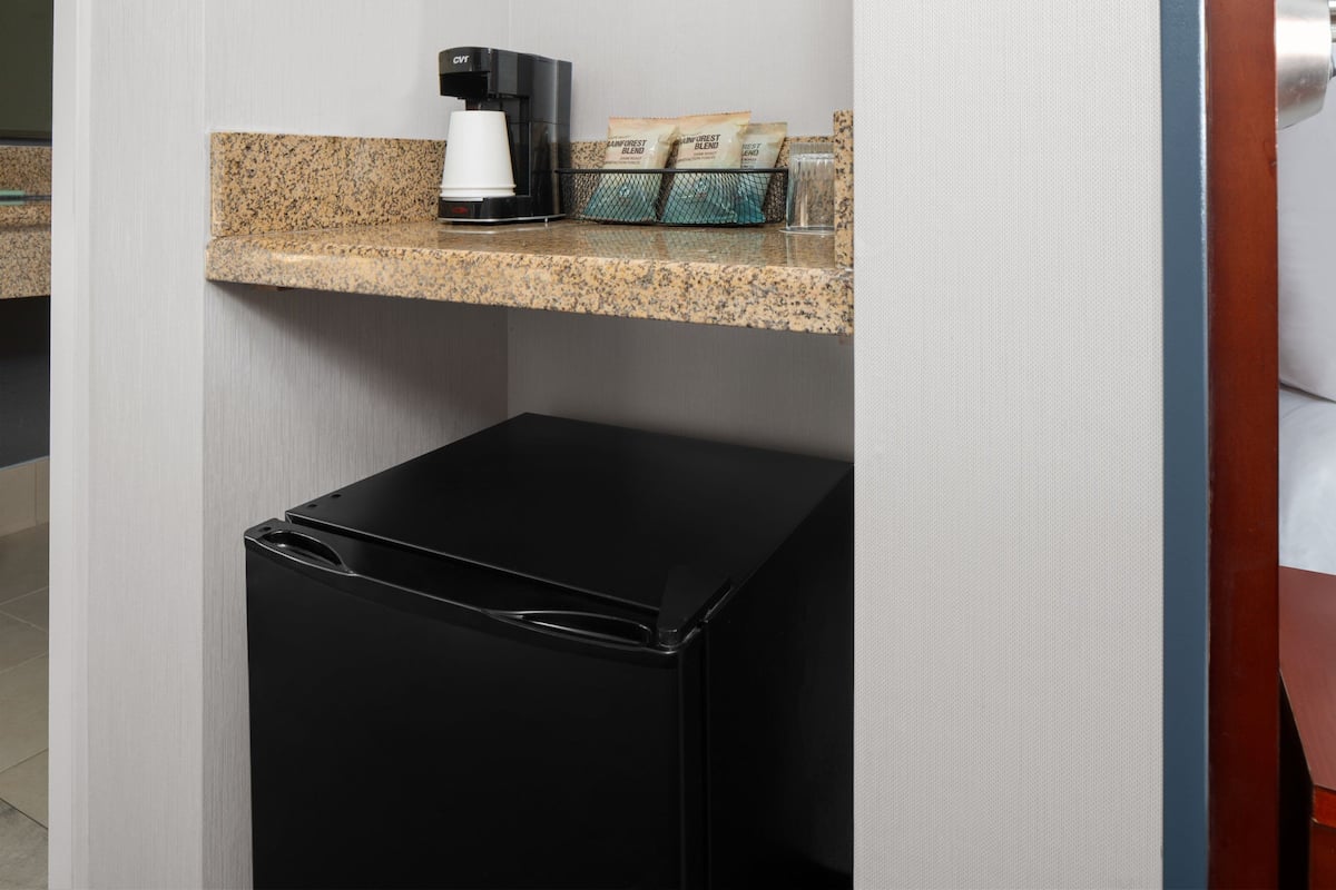 A small black refrigerator, a coffee maker, and a tray with packets on a countertop.