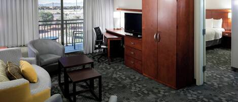 A hotel room with a balcony, a TV, a desk, and a wardrobe.