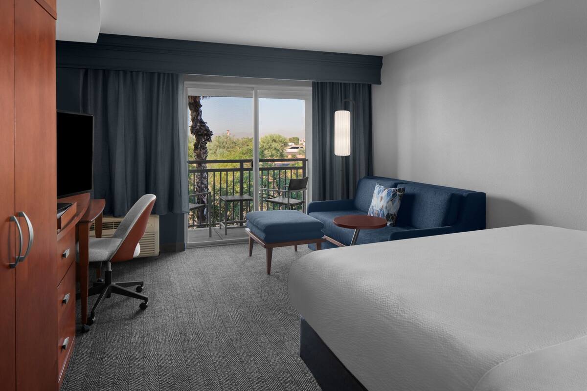 A hotel room with a bed, a desk, a chair, a small table, and a balcony with a view.