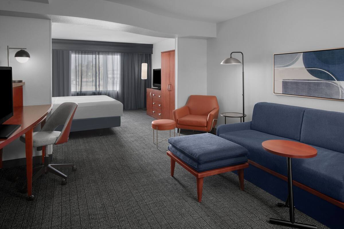 A hotel room with a bed, a desk with a chair, a sofa, a small table, a TV, and a lamp.