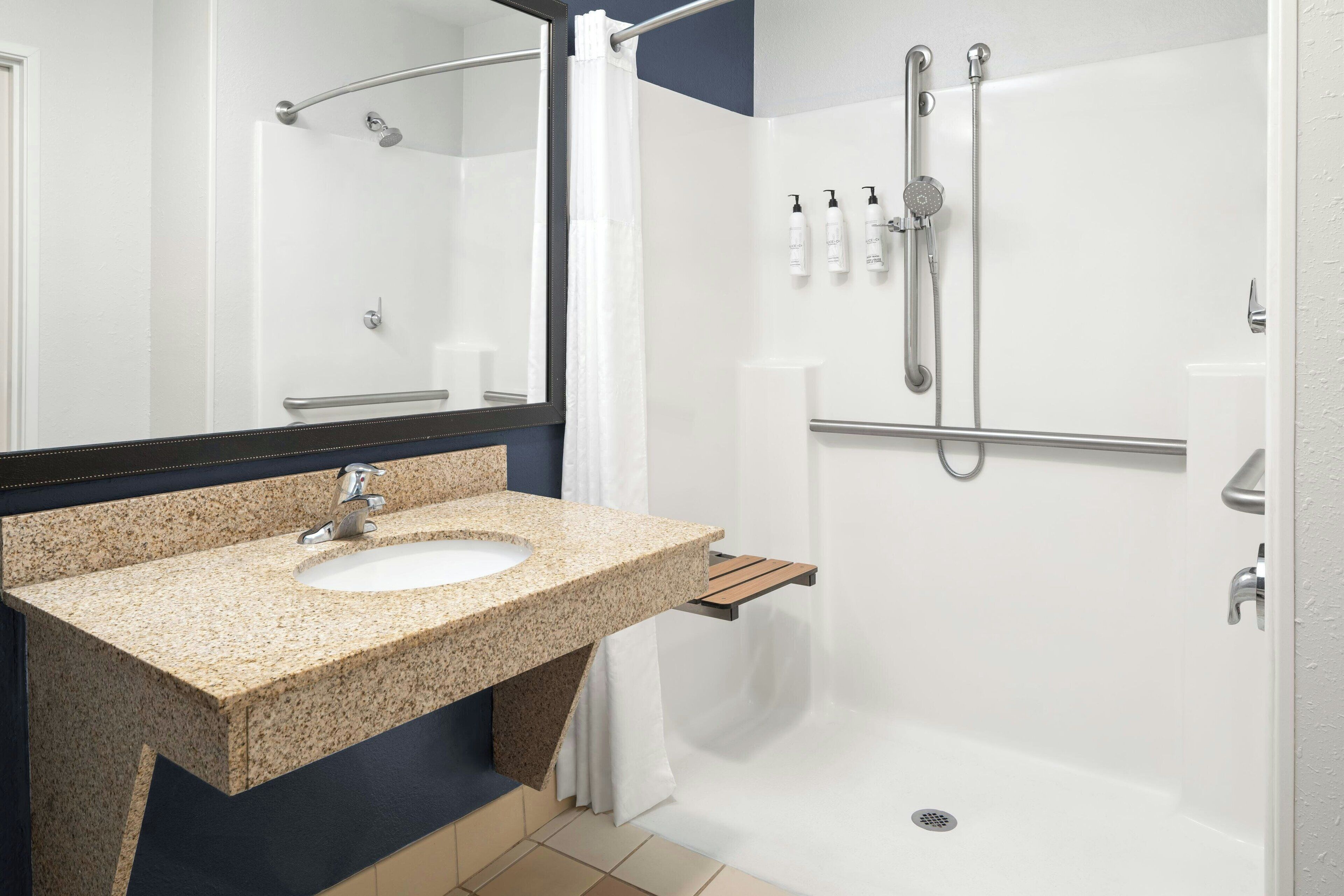 A modern bathroom with a granite sink, a handheld showerhead, and a walk-in shower.