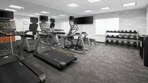 Et fitnessrum med løbebånd, crosstrainere og en væghængt reol med håndvægte.