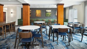 En hotelrestaurant med runde borde og stole, et siddeområde med bænk, samt et gulvtæppe med marmorlook.