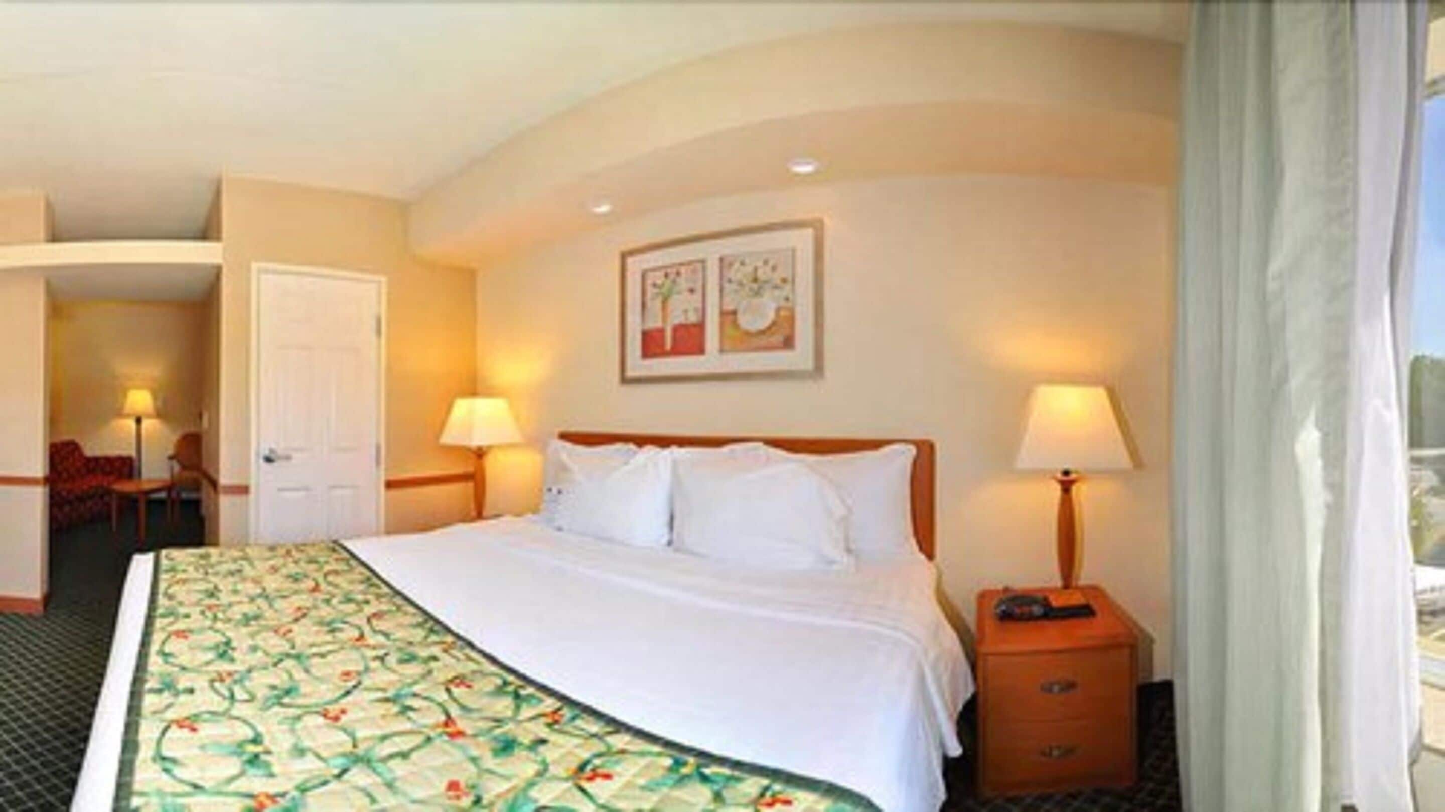 Une chambre d’hôtel comprenant un lit, deux lampes de chevet, une table de chevet, une chaise et une porte donnant sur une autre pièce.