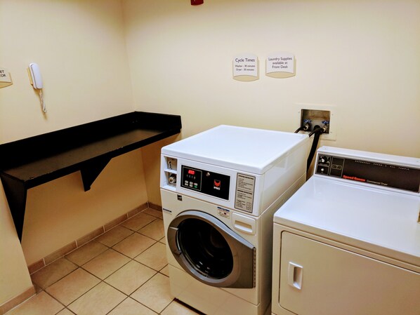 A laundry area with a front-loading washer and dryer, a black shelf, and signs indicating cycle times and laundry supplies availability. - Fairfield Inn & Suites Marianna (Marianna)