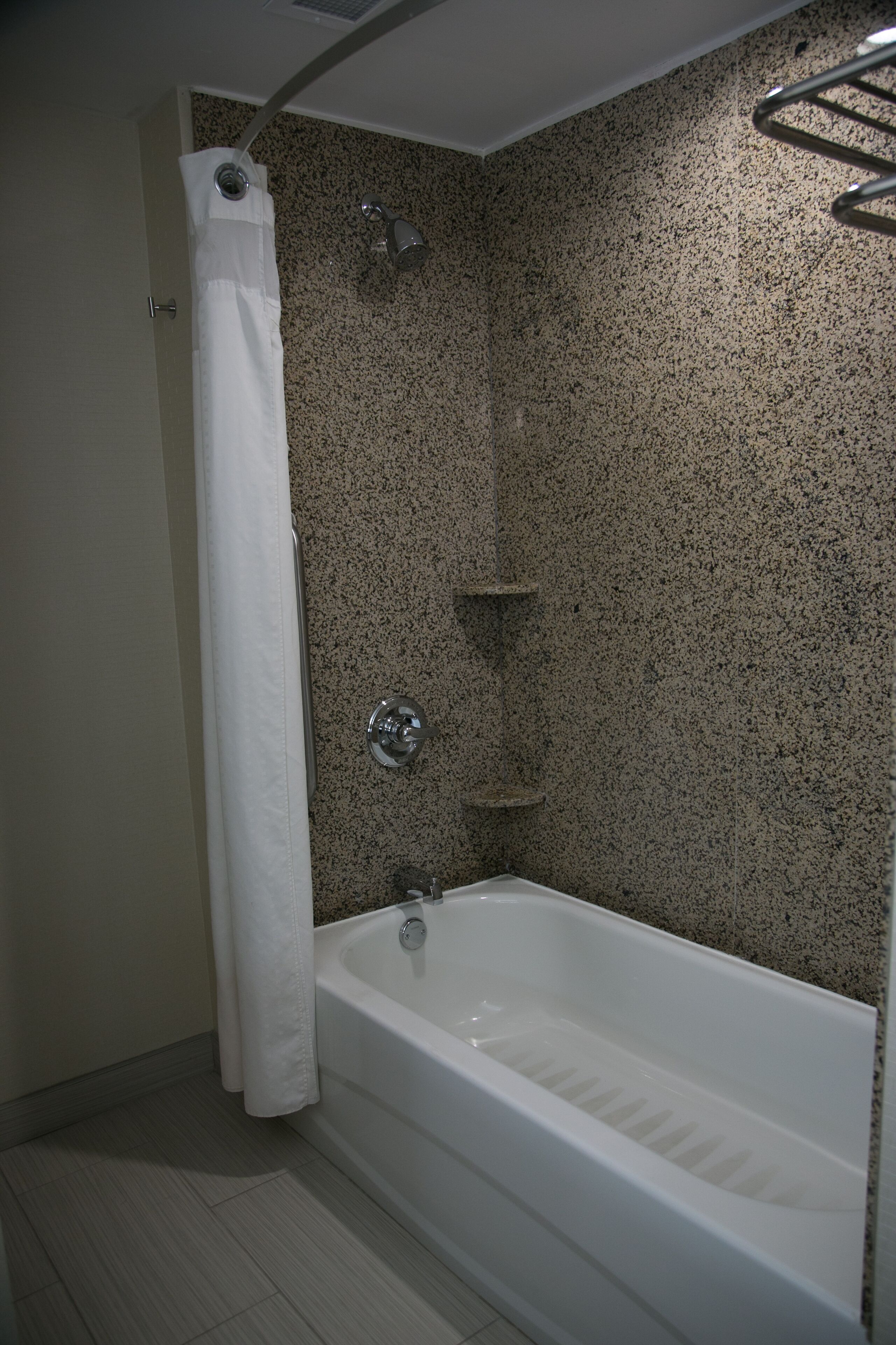 A bathroom with a white bathtub, a shower curtain, and a granite speckled wall.