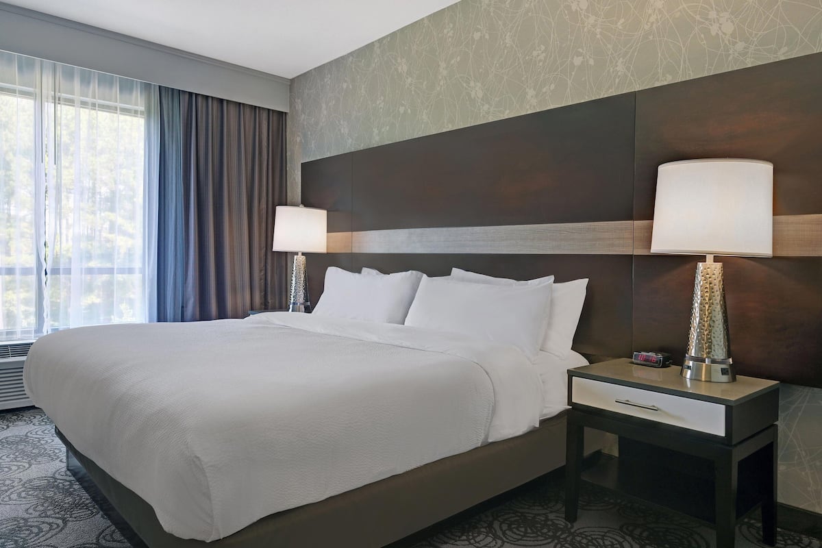 Habitación de hotel con una cama grande, dos lámparas de noche, una mesita de noche y una ventana con cortinas.