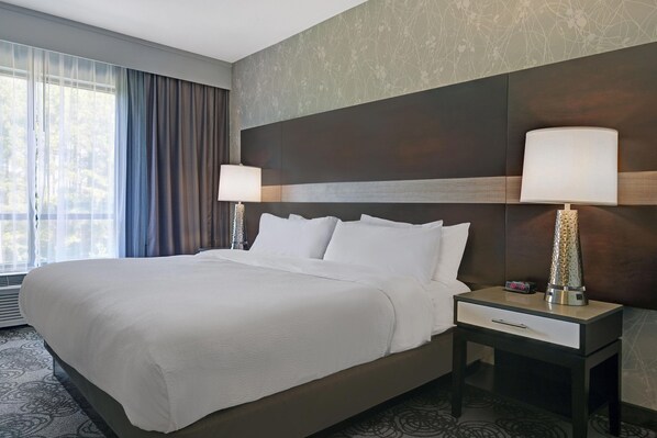A hotel room with a large bed, two bedside lamps, a nightstand, and a window with curtains.