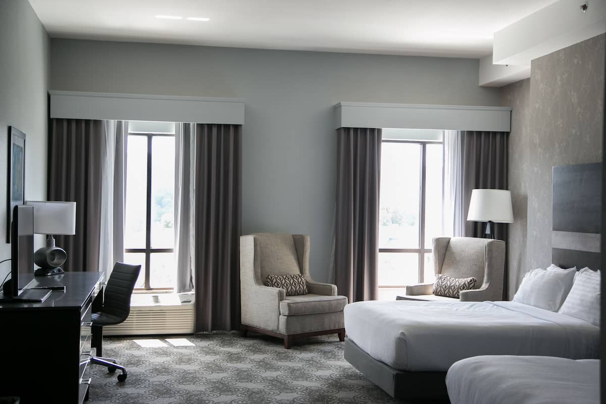 Habitación de hotel con una cama grande, dos sillones, un escritorio con computadora y una ventana con cortinas.