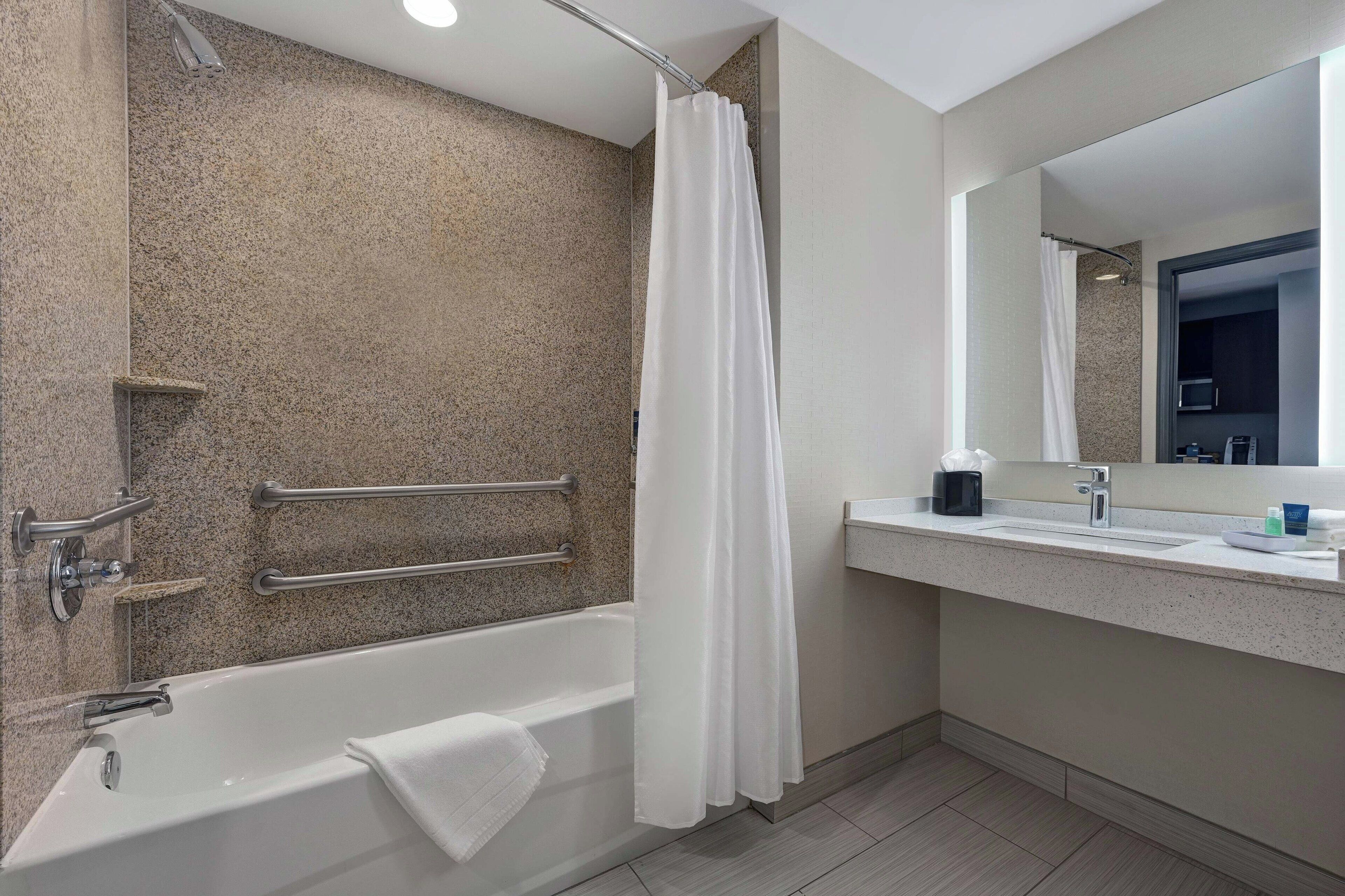 A modern bathroom with a bathtub, a shower curtain, a handrail, a sink, and a mirror.