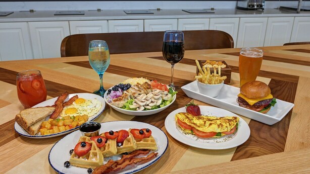 A wooden dining table with various breakfast items including toast, eggs, waffles, and a burger.