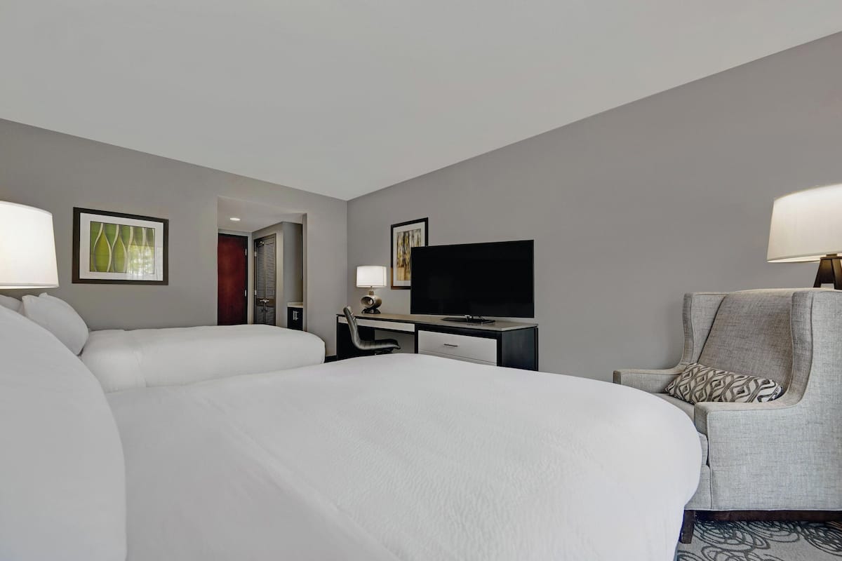 Una habitación de hotel con una cama grande, un escritorio con televisor, una silla y dos mesitas de noche.