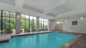 An indoor swimming pool with clear windows, chairs, and a lifeguard warning sign.