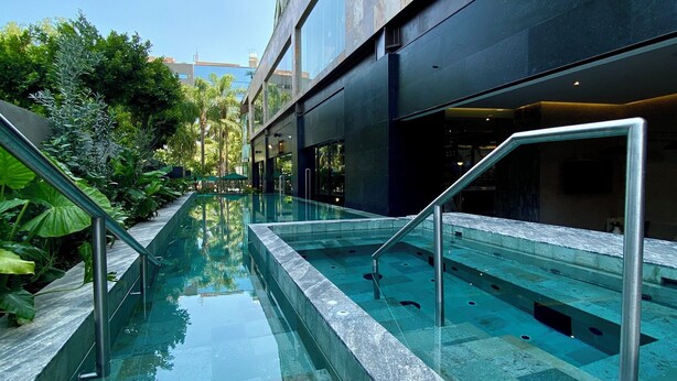 A modern building with a glass-bottomed pool, metal railings, and a clear sky.