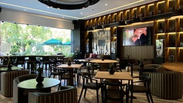 Un restaurante moderno con mesas redondas y cabinas, una pantalla de televisión grande y vistas a zonas verdes al exterior.