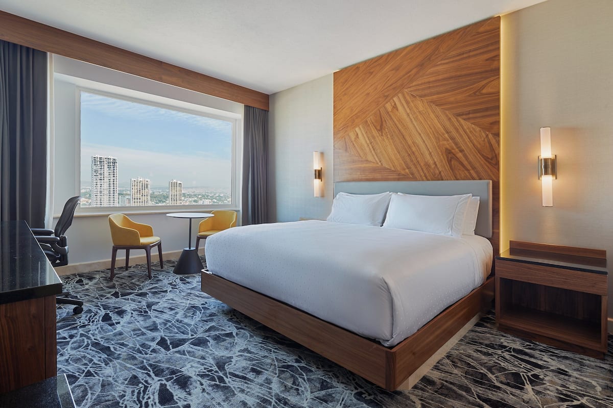 A hotel room with a large bed, a desk, a chair, and a view of the city.