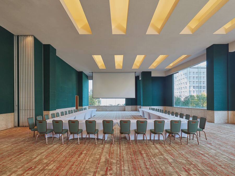 Ein Konferenzraum mit einem langen Tisch, Stühlen und einer großen Leinwand.