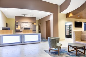 A modern lobby with a reception desk, seating area, and a television screen.