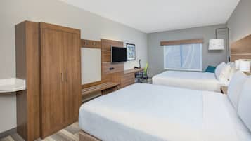 Ett hotellrum med en stor garderob, ett skrivbord med en platt-TV, två sängar, ett fönster med gardiner och ett nattduksbord med en lampa.