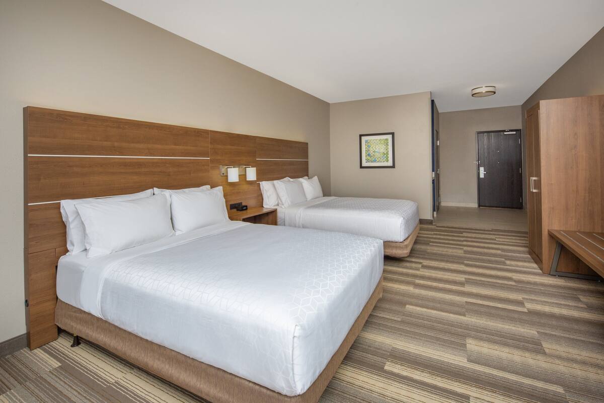 A hotel room with two beds, wooden headboards, a wooden wardrobe, and a framed picture on the wall.