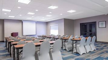 A conference room with rows of tables and chairs, a projector screen, and a presentation screen.