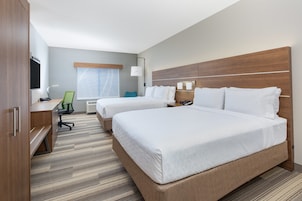 Habitación de hotel con dos camas, un escritorio, una silla, un televisor y un ventanal con cortinas.