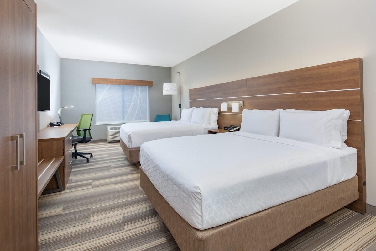 A hotel room with two beds, a desk, a chair, a TV, and a window with curtains.