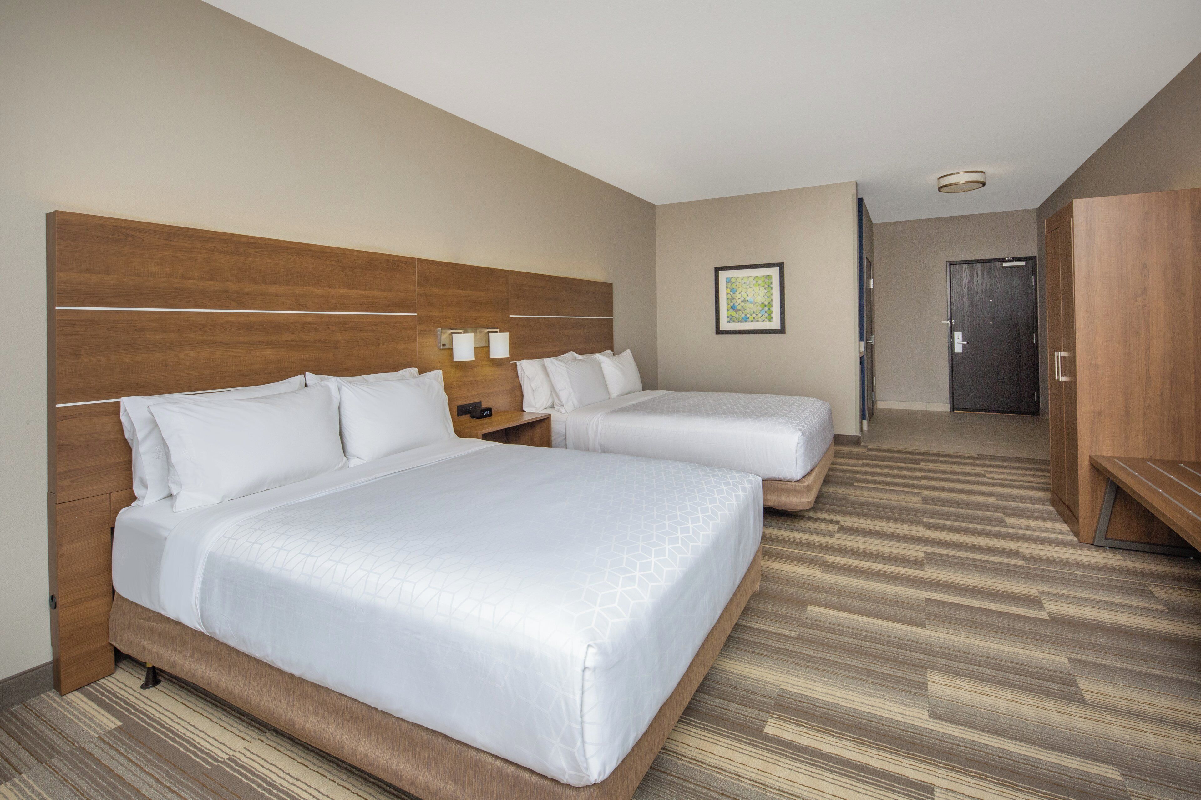 A hotel room with two beds, a wooden headboard, a bedside table with lamps, and a framed picture on the wall.