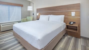 Habitación de hotel con una cama grande, una mesita de noche con un teléfono, una lámpara y una silla.