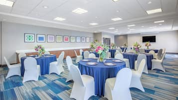 A conference room with round tables, white chairs, and blue tablecloths.