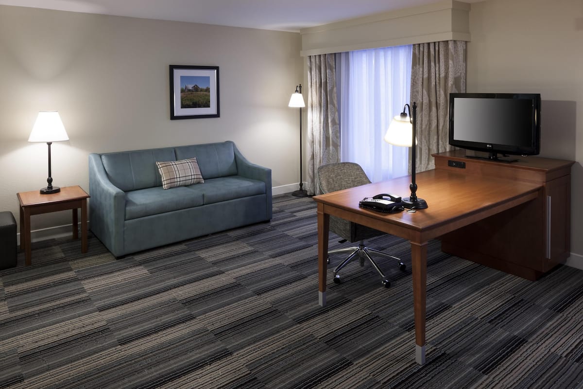 A hotel room with a blue sofa, a wooden desk, a television, two lamps, and a framed picture on the wall.