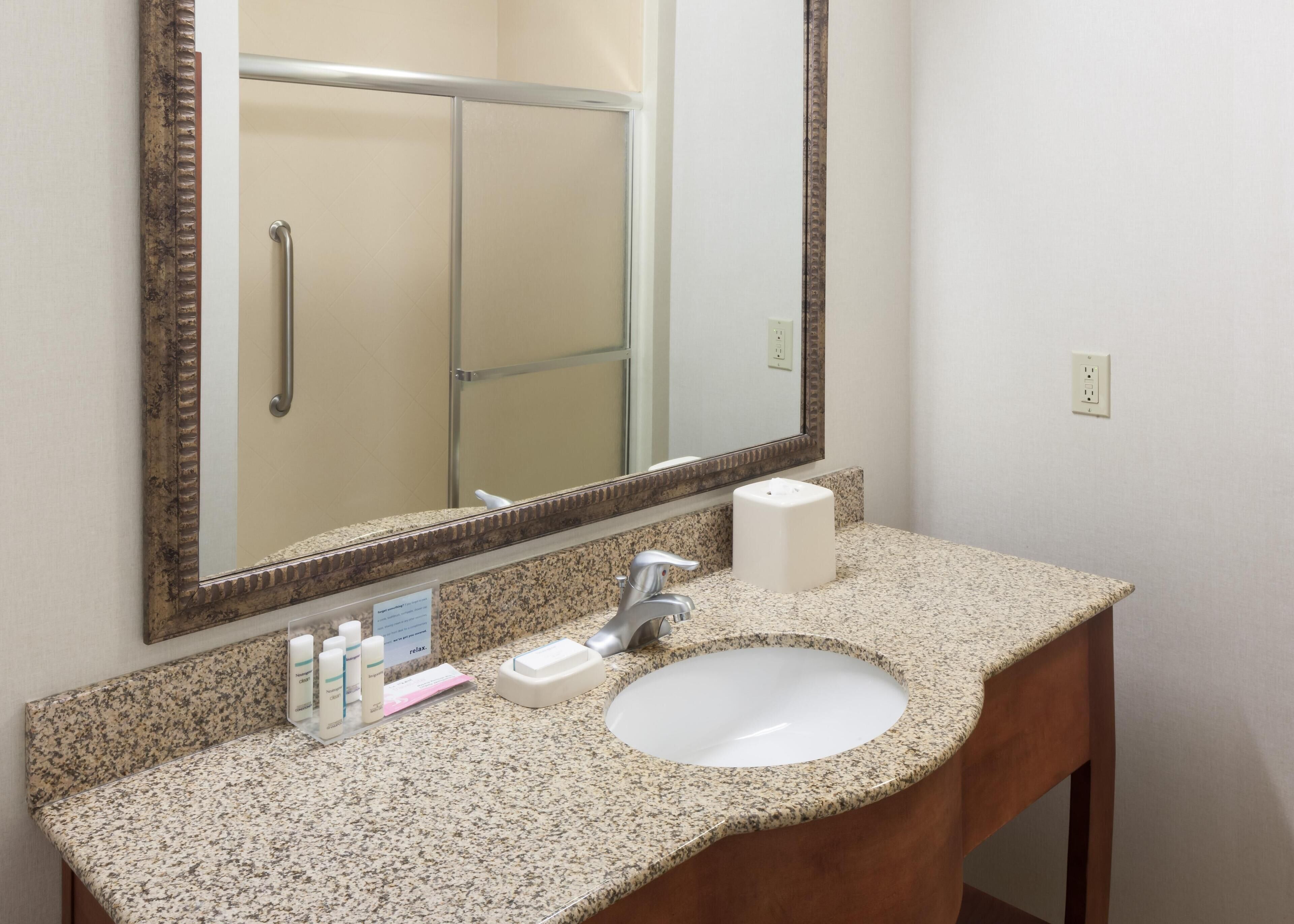 A bathroom with a granite countertop, a white sink, a mirror, and a towel dispenser.