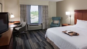 A hotel room with a bed, a desk with a computer, a chair, a TV, and a window with curtains. - Hampton Inn & Suites Davenport (Davenport)