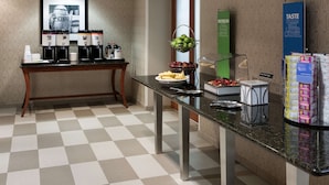 A hotel reception area with a checkered floor, a reception desk, coffee machines, a fruit bowl, a green sign, and a buffet display. - Hampton Inn & Suites Davenport (Davenport)