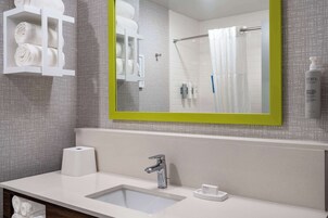 Un baño moderno con un lavabo blanco, un espejo de marco verde y un perchero con toallas dobladas.