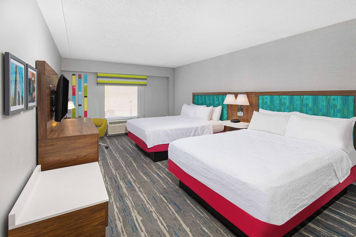 A hotel room with two beds, a desk, a chair, and a TV.