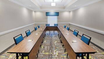 A conference room with a long table, blue chairs, and a patterned carpet.
