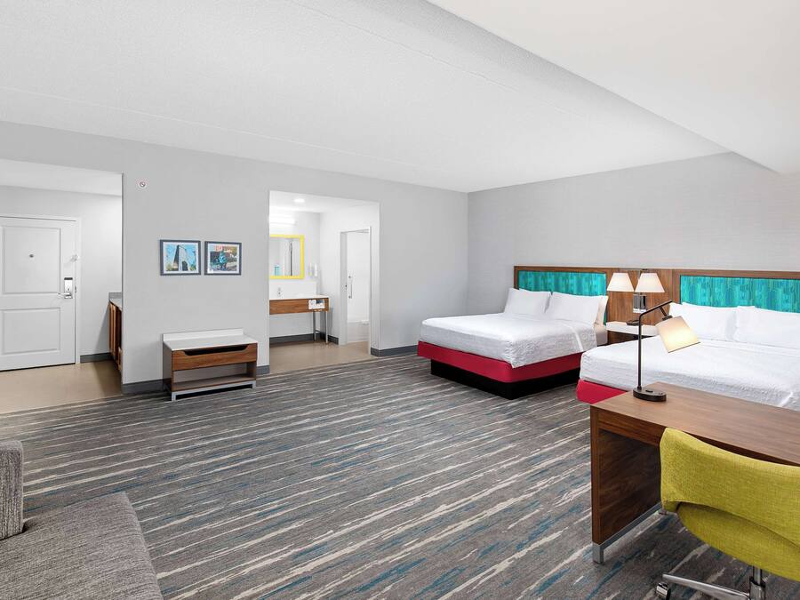 Ein Hotelzimmer mit zwei Betten, einem Schreibtisch, einem Stuhl, einem kleinen Tisch und einem Spiegel.