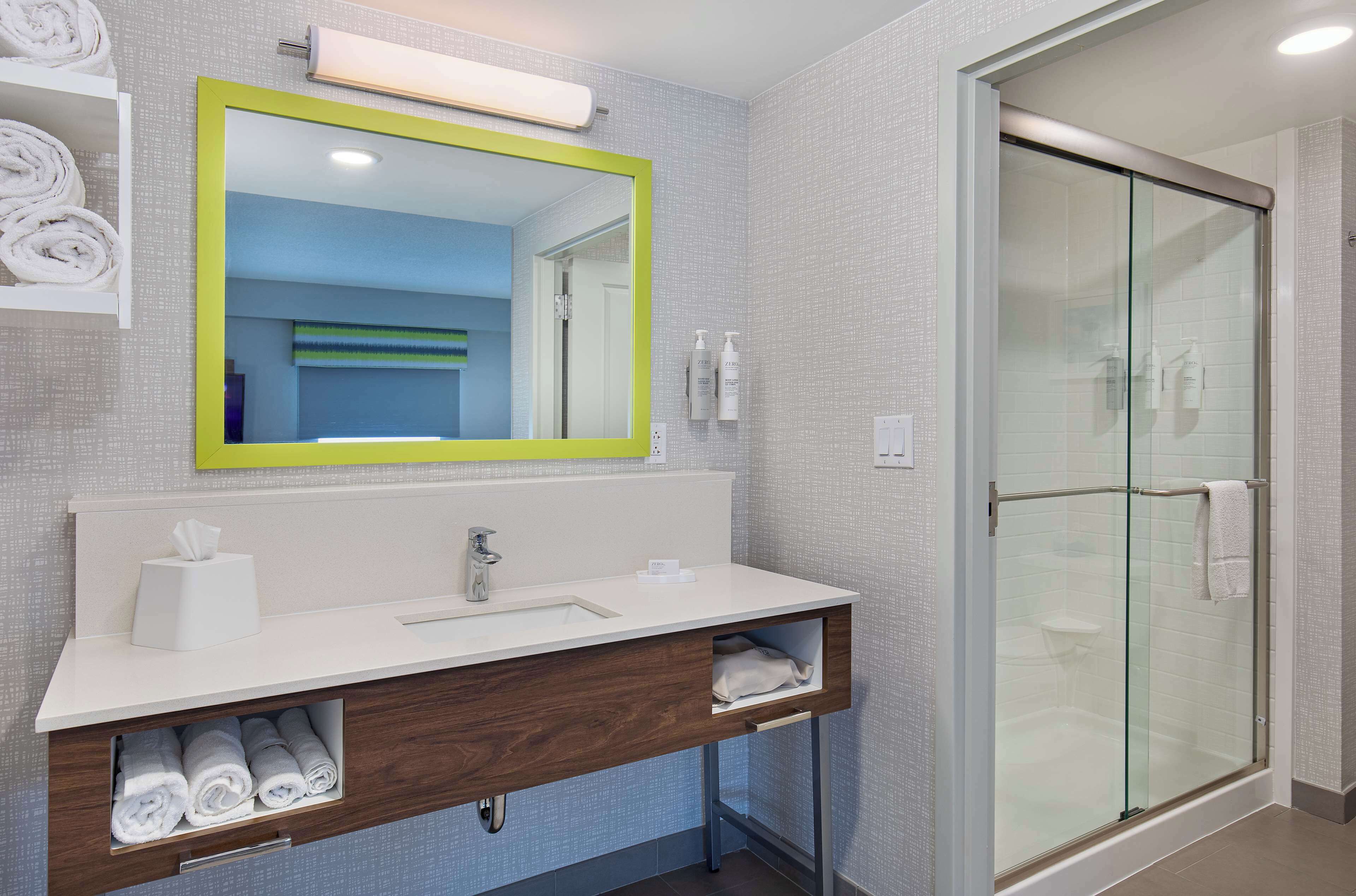 Casa de banho moderna com lavatório branco, espelho com moldura verde e cabine de duche em vidro.