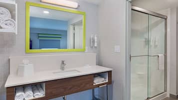 Casa de banho moderna com lavatório branco, espelho com moldura verde e cabine de duche em vidro.