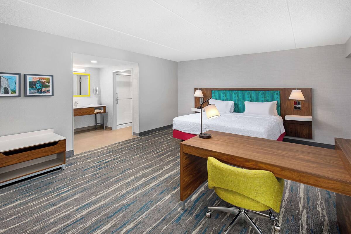 A hotel room with a bed, bedside tables, a desk, a chair, and a bathroom visible through an open door.