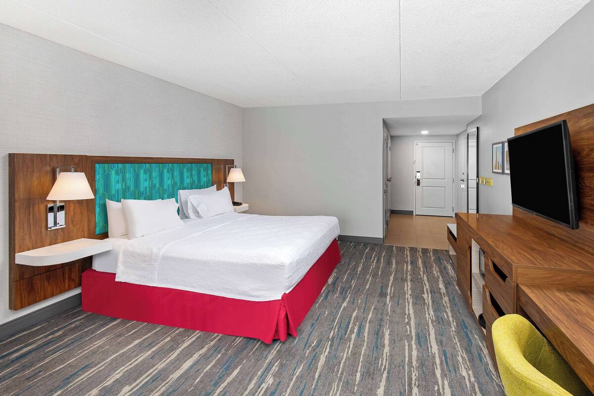 A hotel room with a bed, bedside tables, a TV, and a desk.