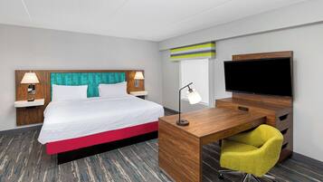 A hotel room with a bed, a desk, a chair, a TV, and a window.