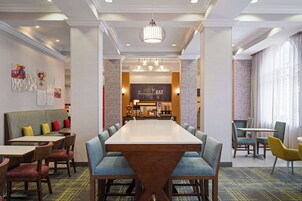 A hotel dining area with a long table, multiple chairs, and a central chandelier.