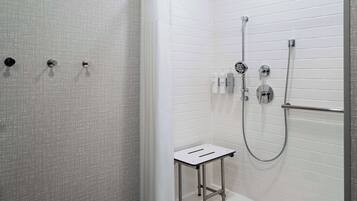 A modern bathroom with white tiled walls, a shower with a handheld showerhead, and a small white stool.