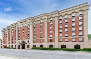 A large, multi-story hotel with a classic architectural design, featuring a prominent American flag and a sign reading "Hampton Inn."