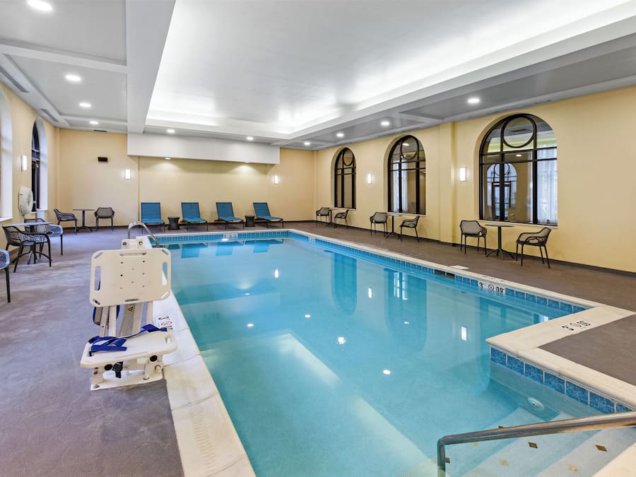 A swimming pool with lounge chairs and tables, a lifeguard chair, and arched windows.