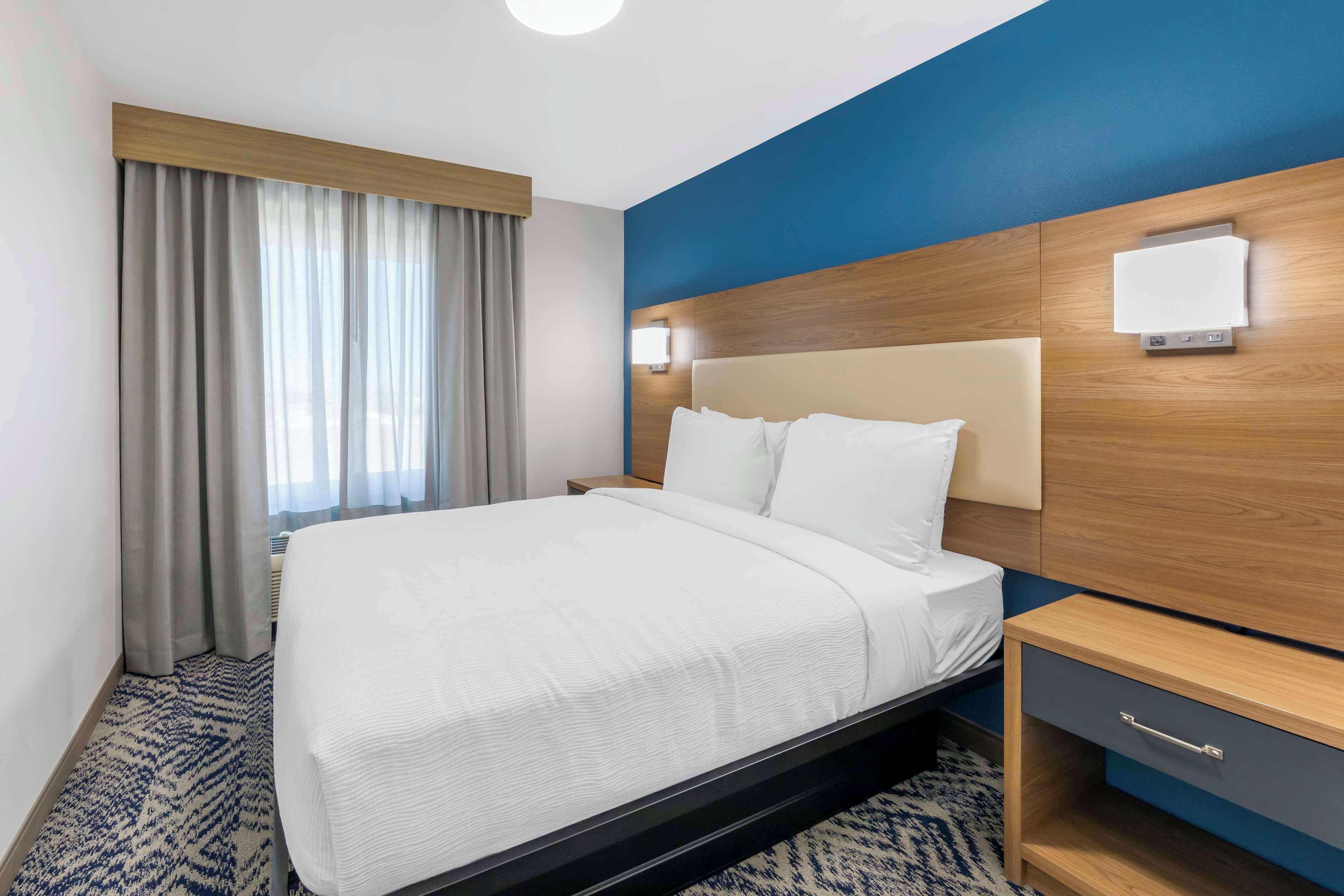 Camera d'albergo con un letto, un comodino, una lampada a parete e una finestra con tende.
