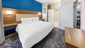 A hotel room with a large bed, a nightstand, a wooden headboard, a wall-mounted light, and a door leading to a closet. - Executive Residency by Best Western Victorville (Victorville)